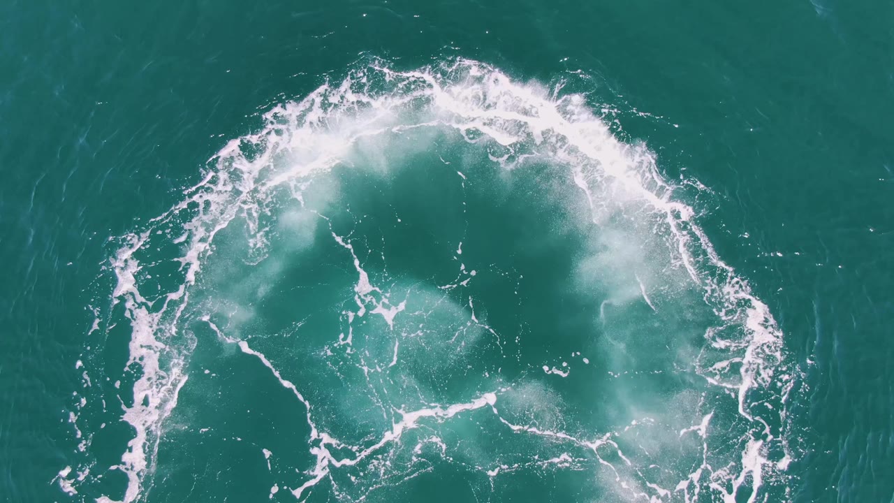 Circular white foam wake on turquoise ocean water.