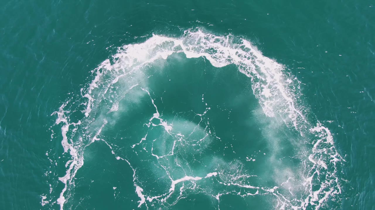 At one second, the overhead Buzzards Beach frame shows the circular wake still bright, with the lower foam lines thinning inside the turquoise water and no visible people.