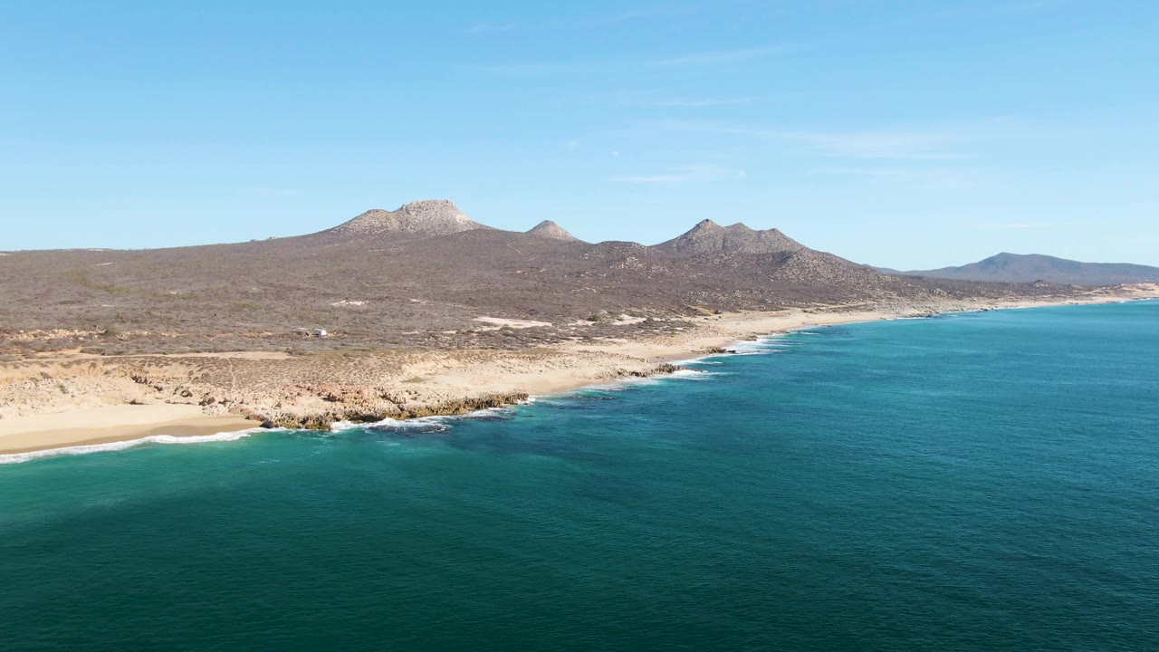 Aerial coastline with turquoise water, sandy shore, and distant mountains.