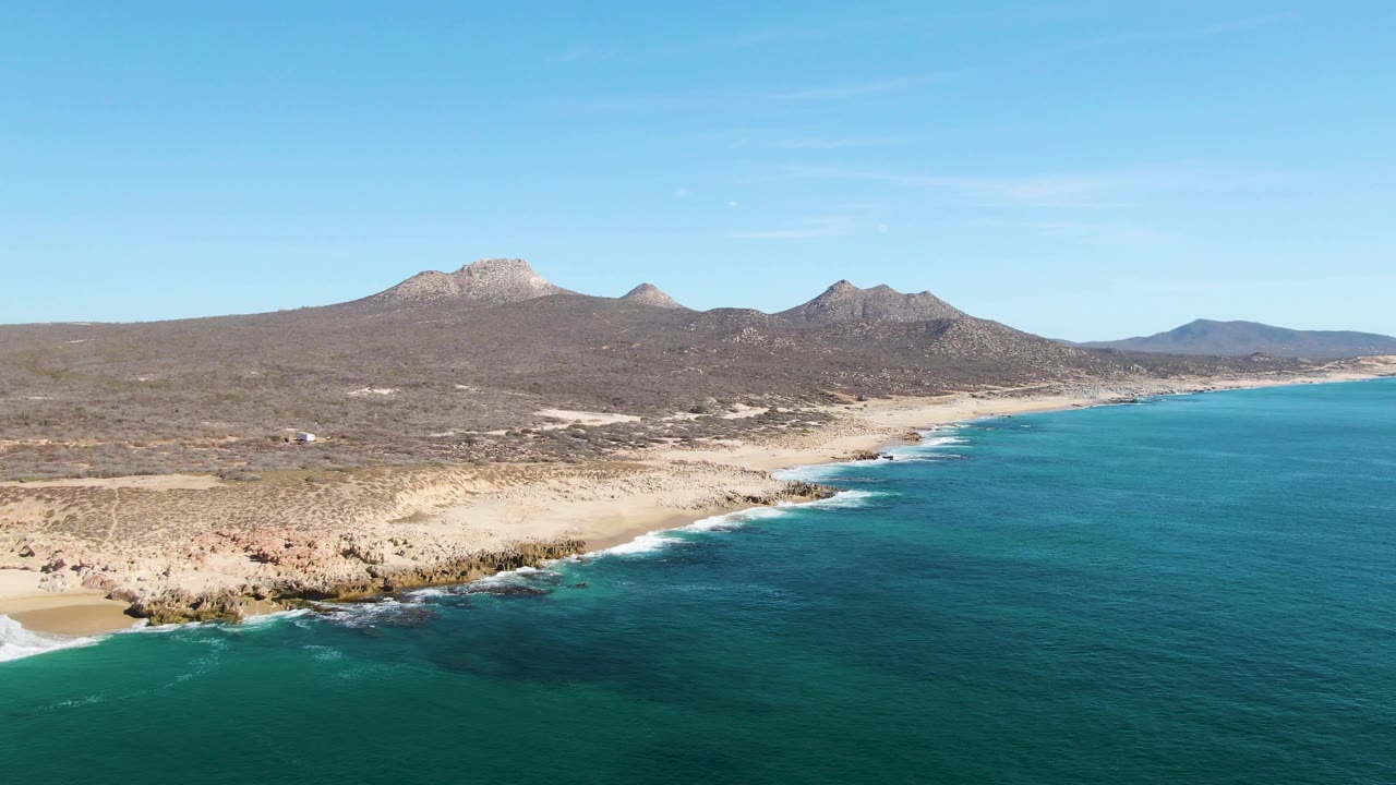 Rocky beach and teal ocean seen from above with mountains beyond the shore.