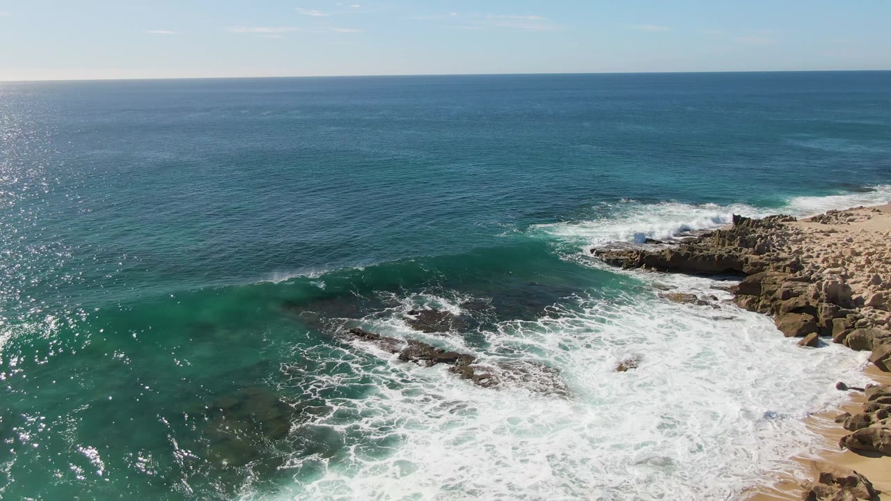 Foamy surf covers the lower shoreline beneath clear turquoise water.