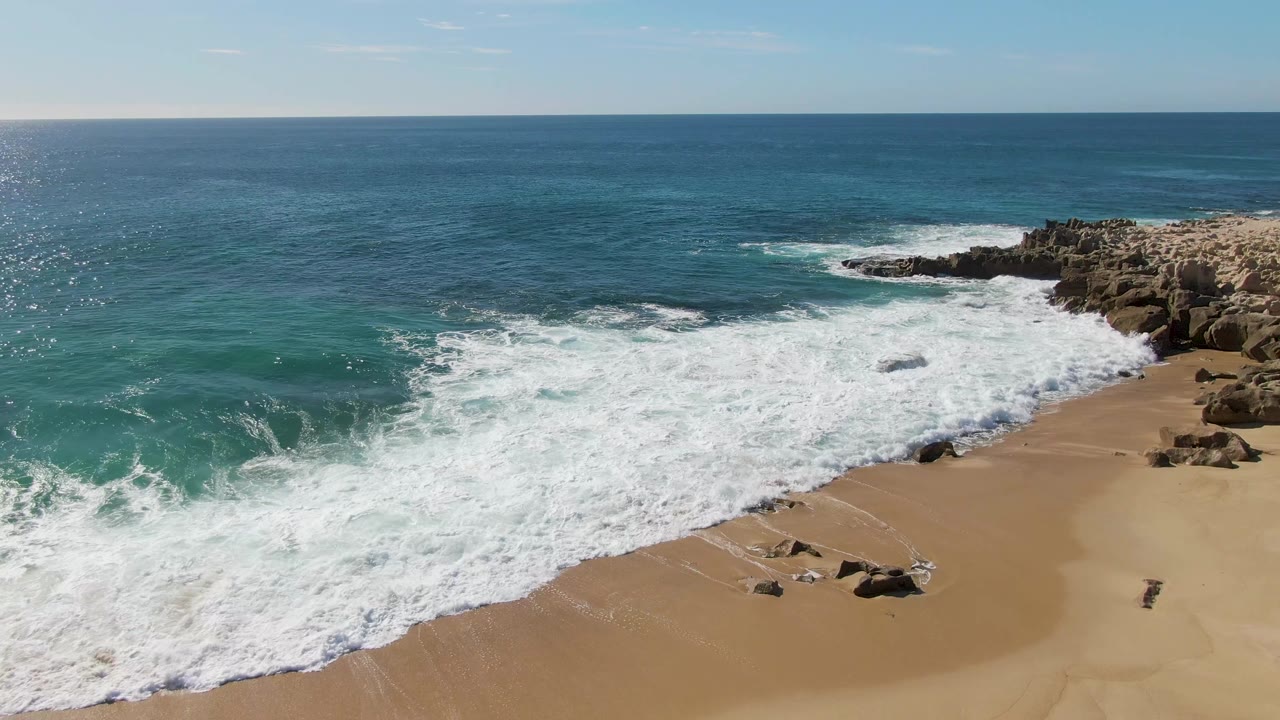 Aerial view of waves breaking onto a sandy beach beside rocky outcrops.
