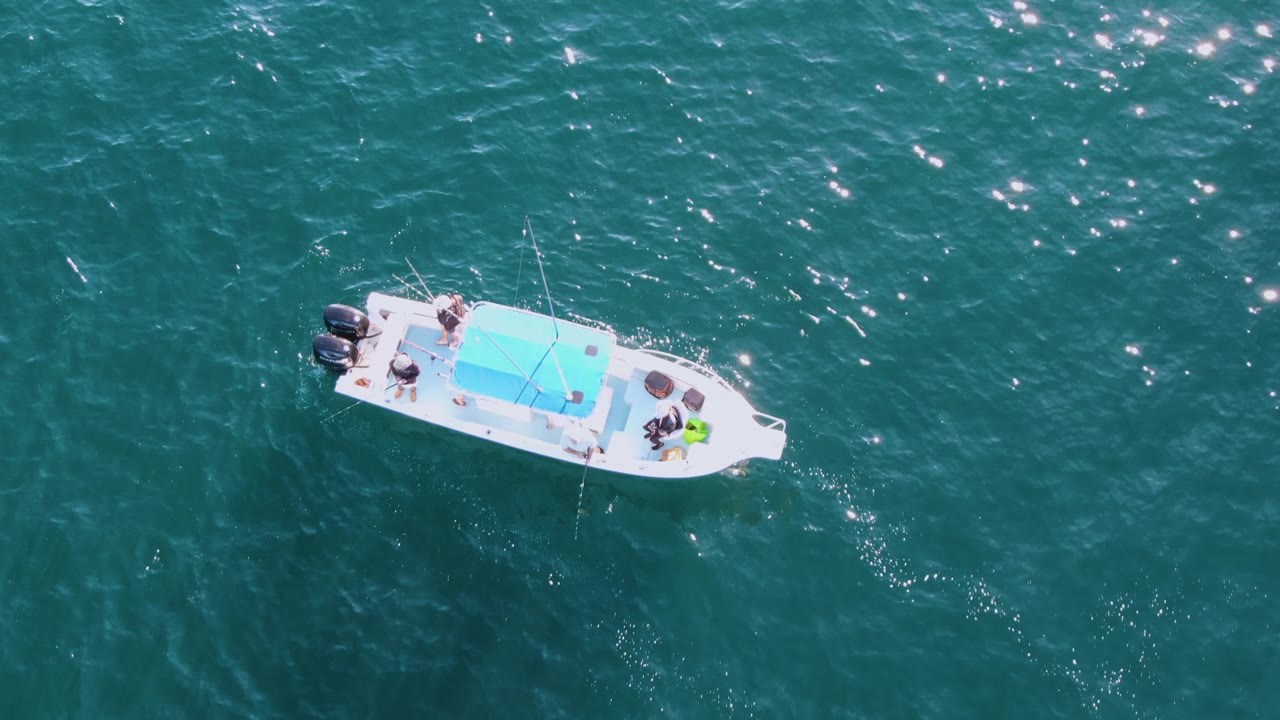 Small white boat centered over rippled teal water.