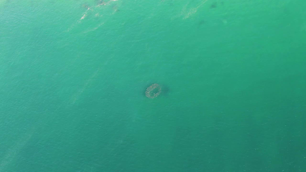 Buzzards Beach ocean water seen from above, with the circular submerged pattern low and left and small surface ripples crossing the frame, no visible people.