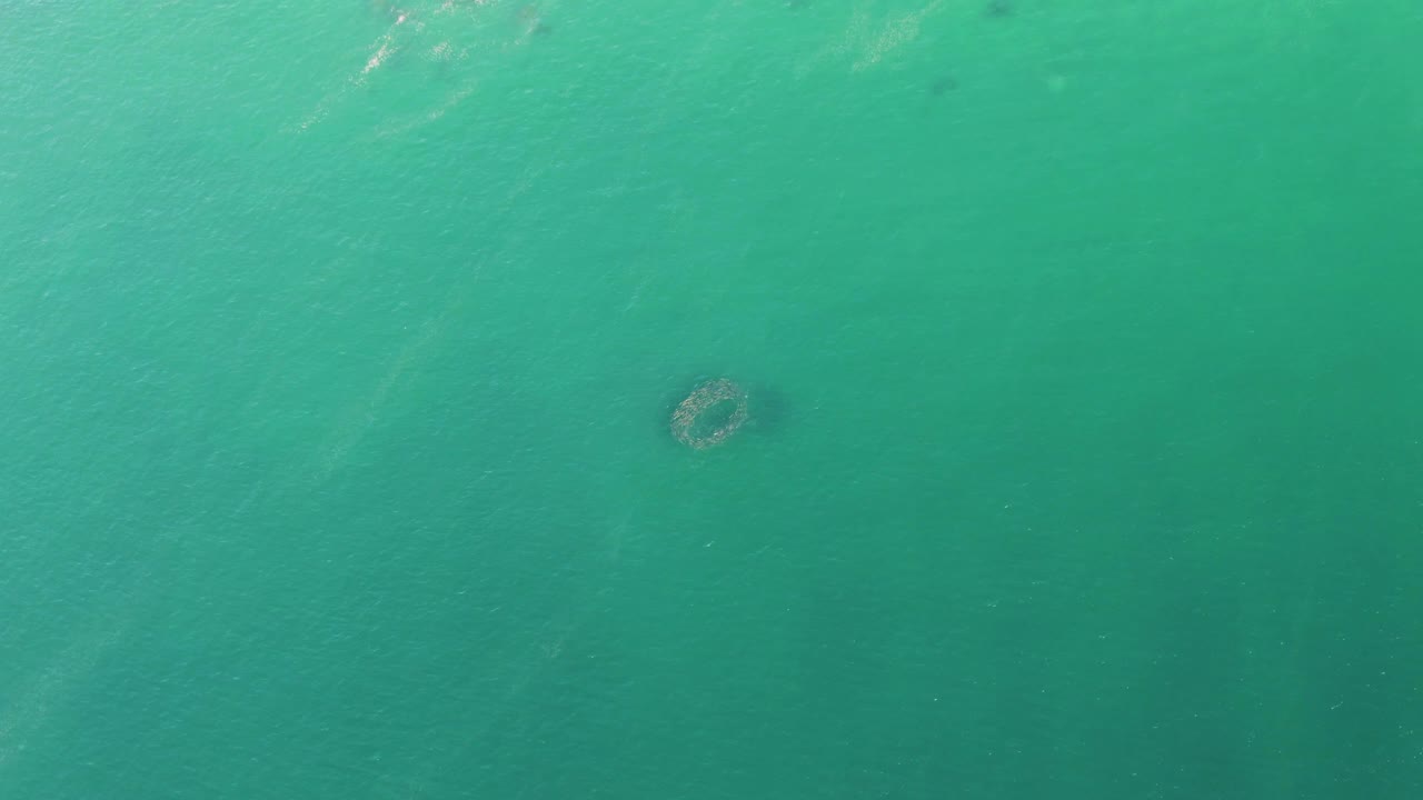 Overhead view of turquoise water at Buzzards Beach, Baja California Sur, with a small circular underwater formation left of center and no visible people.