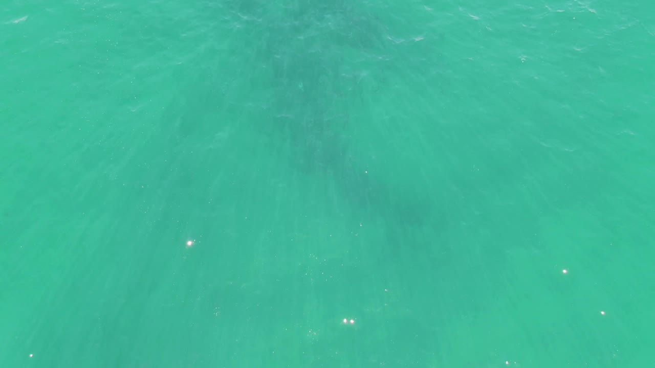 Shallow turquoise ocean at Buzzards Beach with darker underwater streaks visible through the clear surface and no visible people.