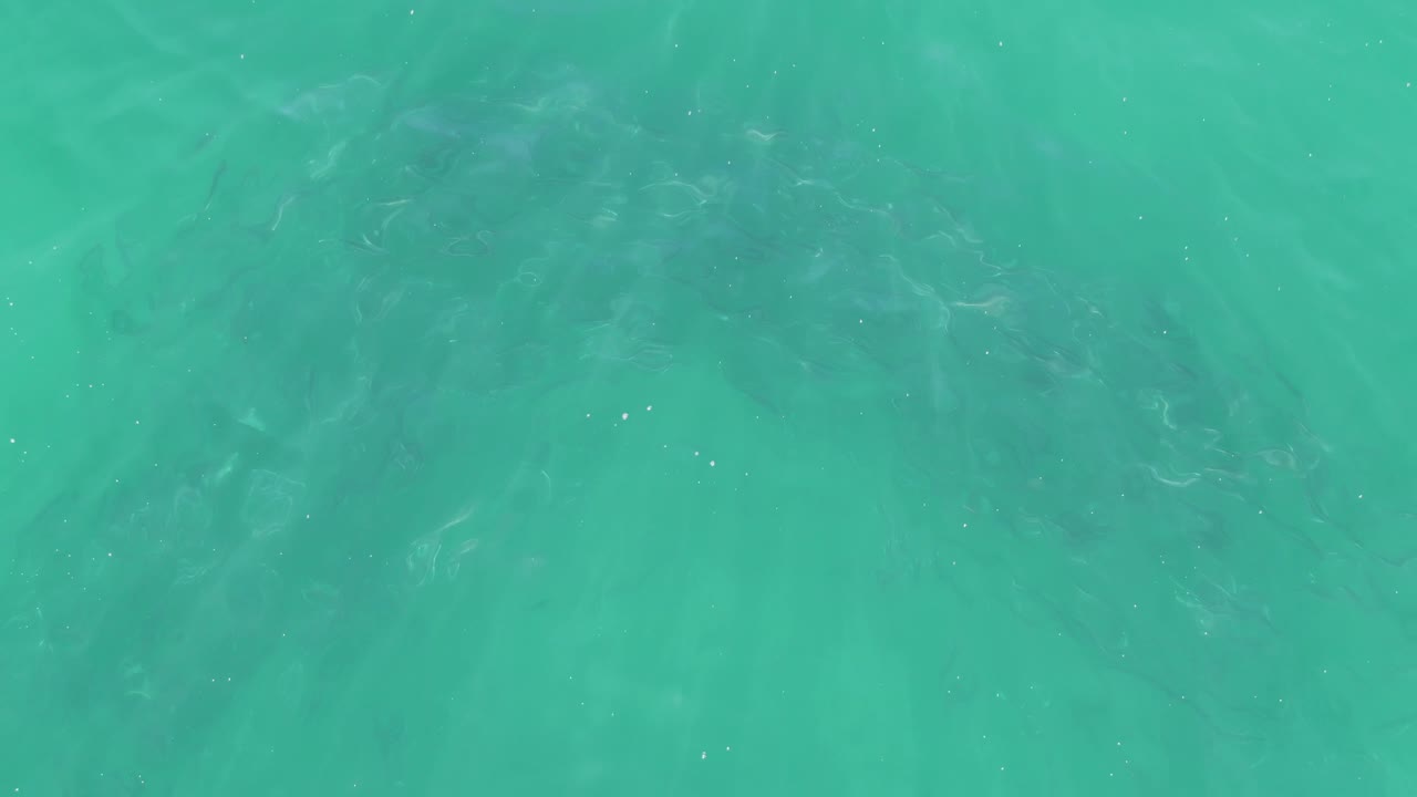 Turquoise sea surface at Buzzards Beach in Baja California Sur, with soft reflected light and darker underwater shapes concentrated near the top, no visible people.