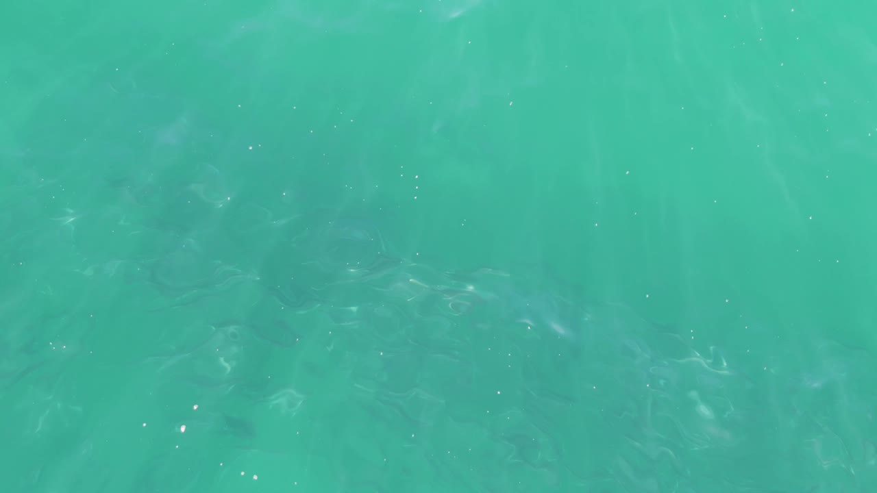 Turquoise ocean water with soft ripples and faint darker patches below the surface.