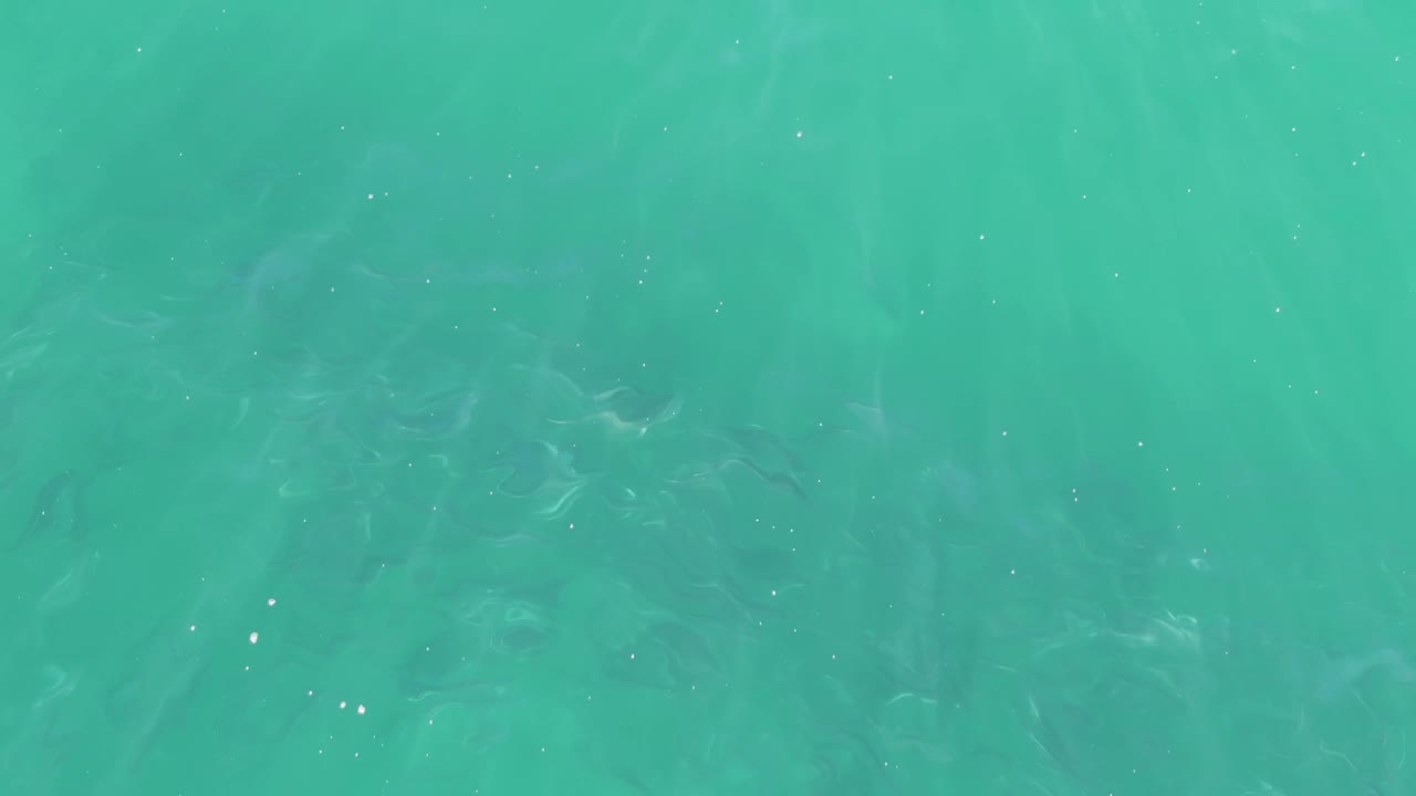 Clear green-blue ocean water at Buzzards Beach with subtle ripples crossing the frame, a few small white reflections, and no visible people.