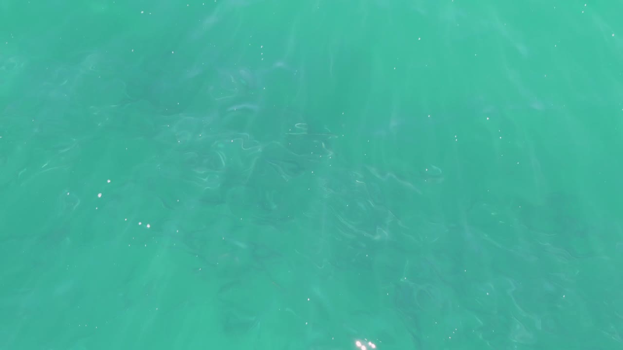 Top-down view of Buzzards Beach turquoise water with scattered bright sparkles, soft wave texture across the surface, and no visible people.