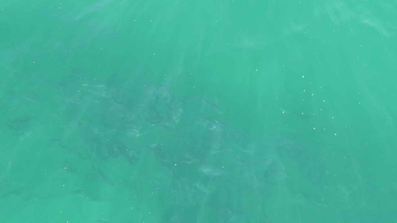 Clear teal water fills the frame at Buzzards Beach, Baja California Sur, with soft ripples and darker underwater patches, no visible people.