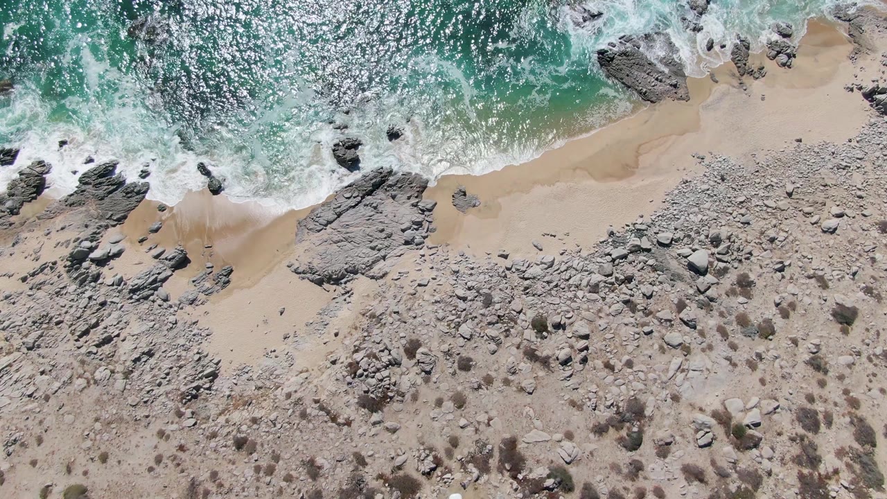 Turquoise waves breaking over sand and rocks from an overhead view