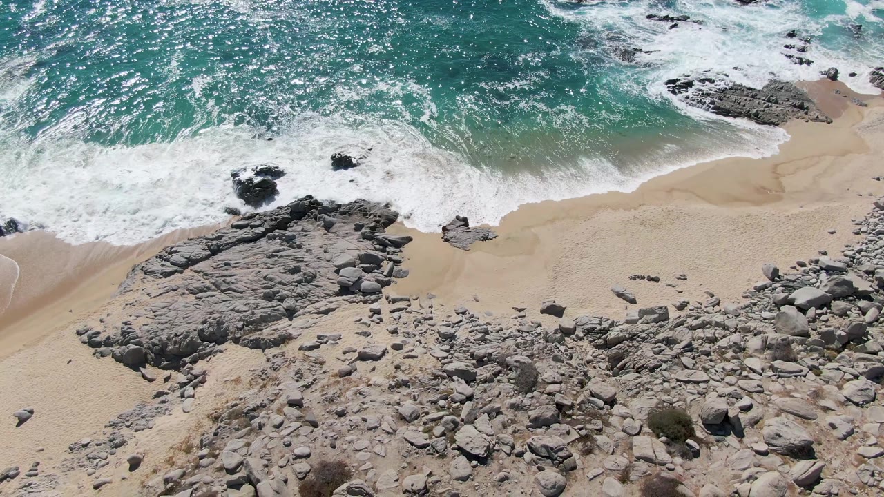 Rocky foreground below surf washing onto sand