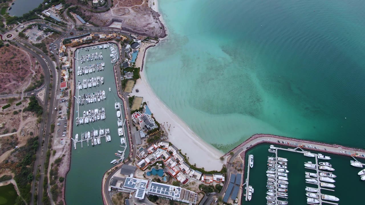 Aerial coastal marina beside a pale beach and open water