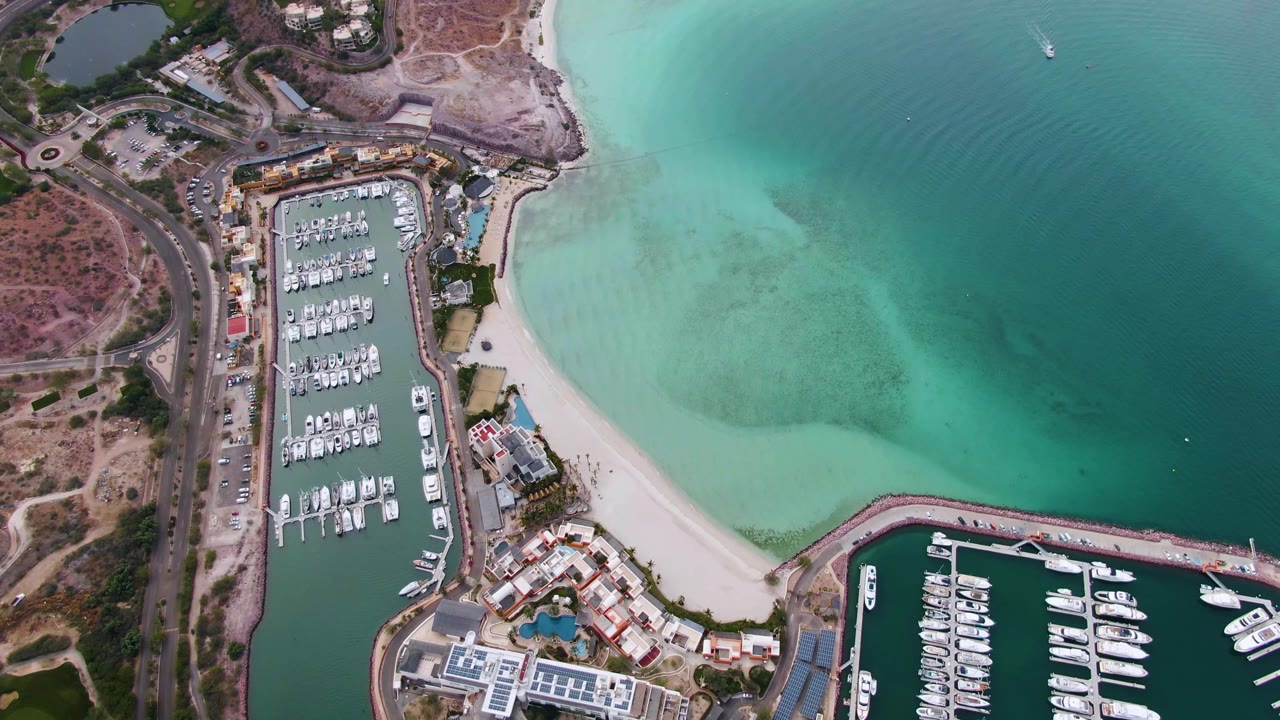 Aerial view of docked boats, beach, and shifting blue-green water.