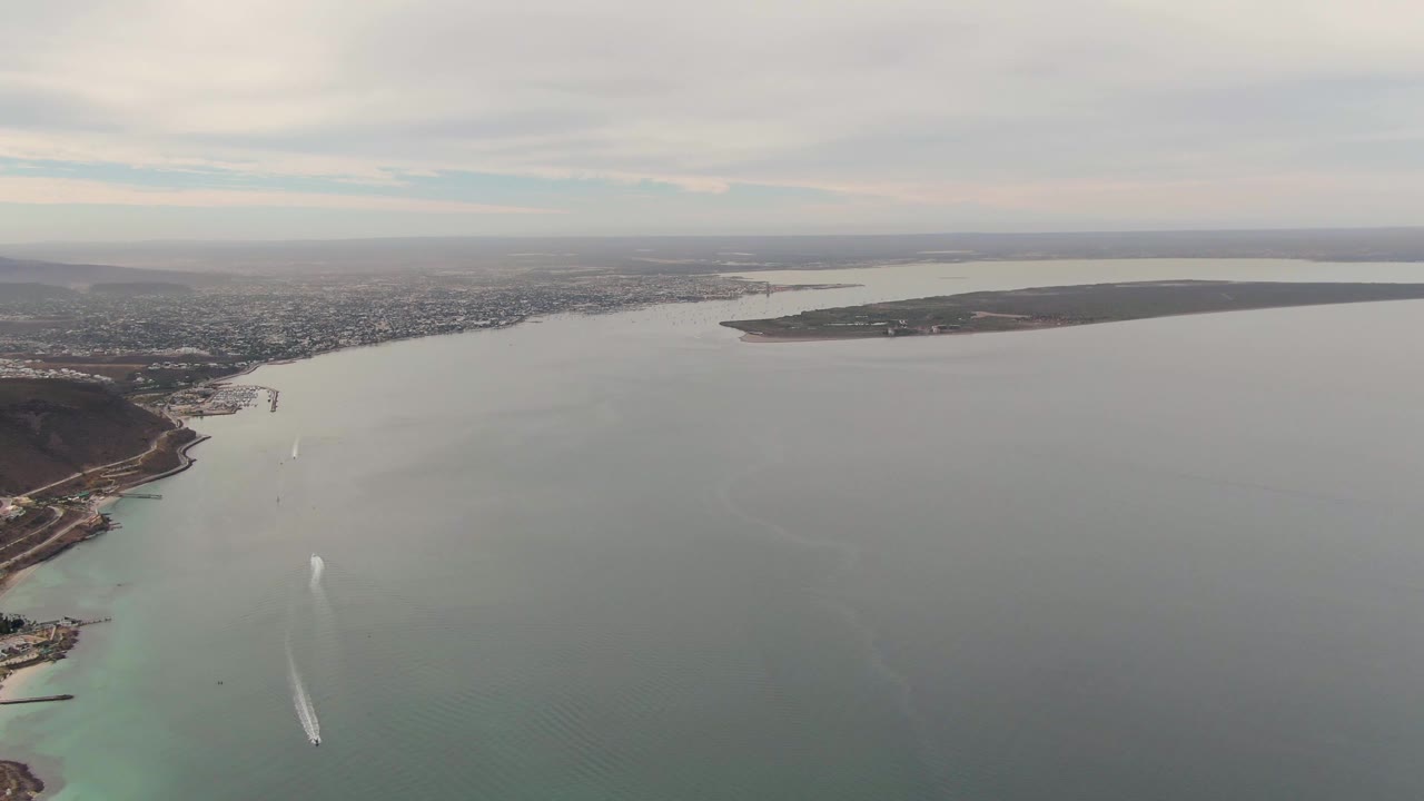 High aerial view of a boat wake crossing open coastal water near land.