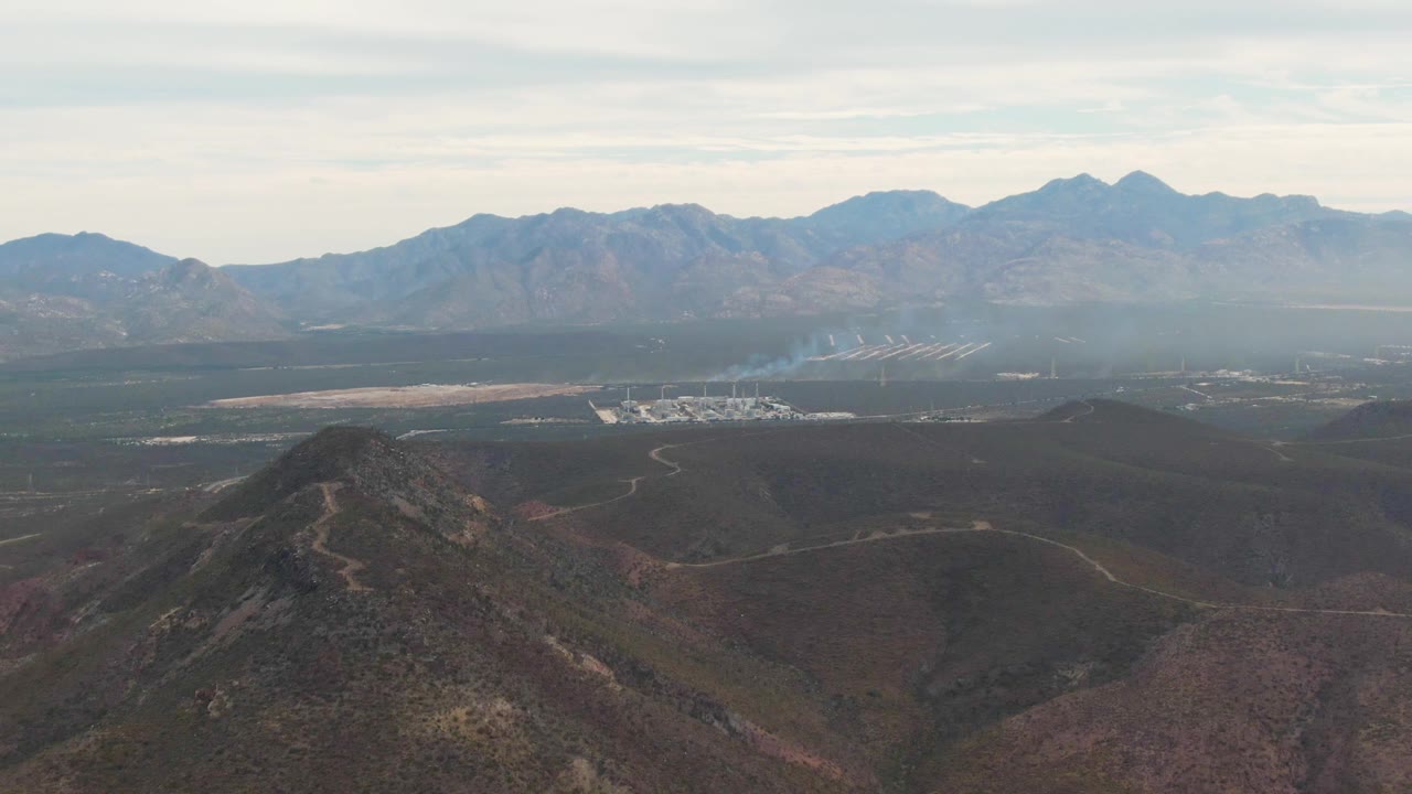 Aerial valley landscape with smoke rising below distant mountains.