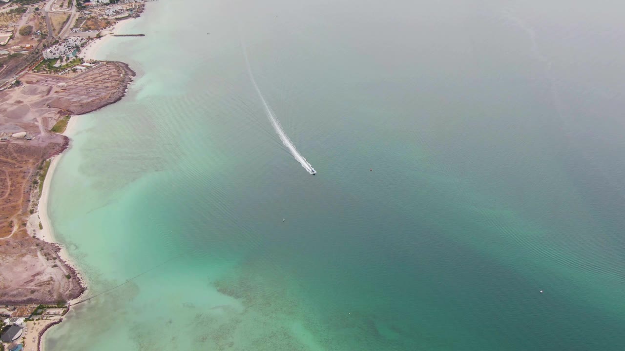 Aerial view in La Paz, Baja California Sur, with the boat farther into open green-blue water and a curved white wake trailing behind it, no visible people.