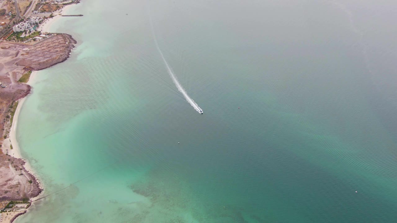 Aerial frame from La Paz, Baja California Sur, showing the boat near the right side of the water field while the shoreline remains at the upper left, with no visible people.
