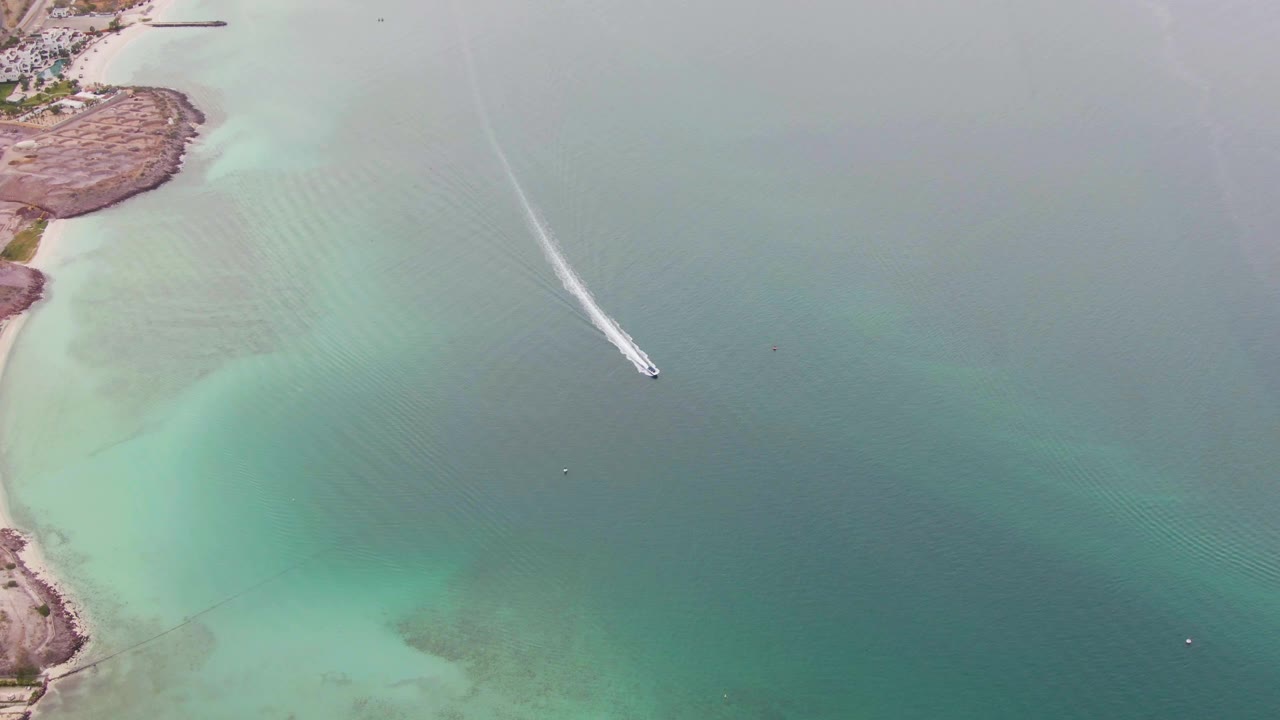 Aerial La Paz, Baja California Sur frame with the boat and white wake crossing the central water area, pale shallows to the left, and no visible people.
