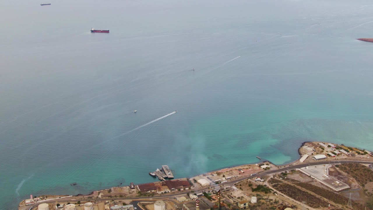 Drone aerial over La Paz, Baja California Sur, showing the port-side shoreline lower in frame, blue-green water, anchored ships near the horizon, a speedboat trail, and no visible people.