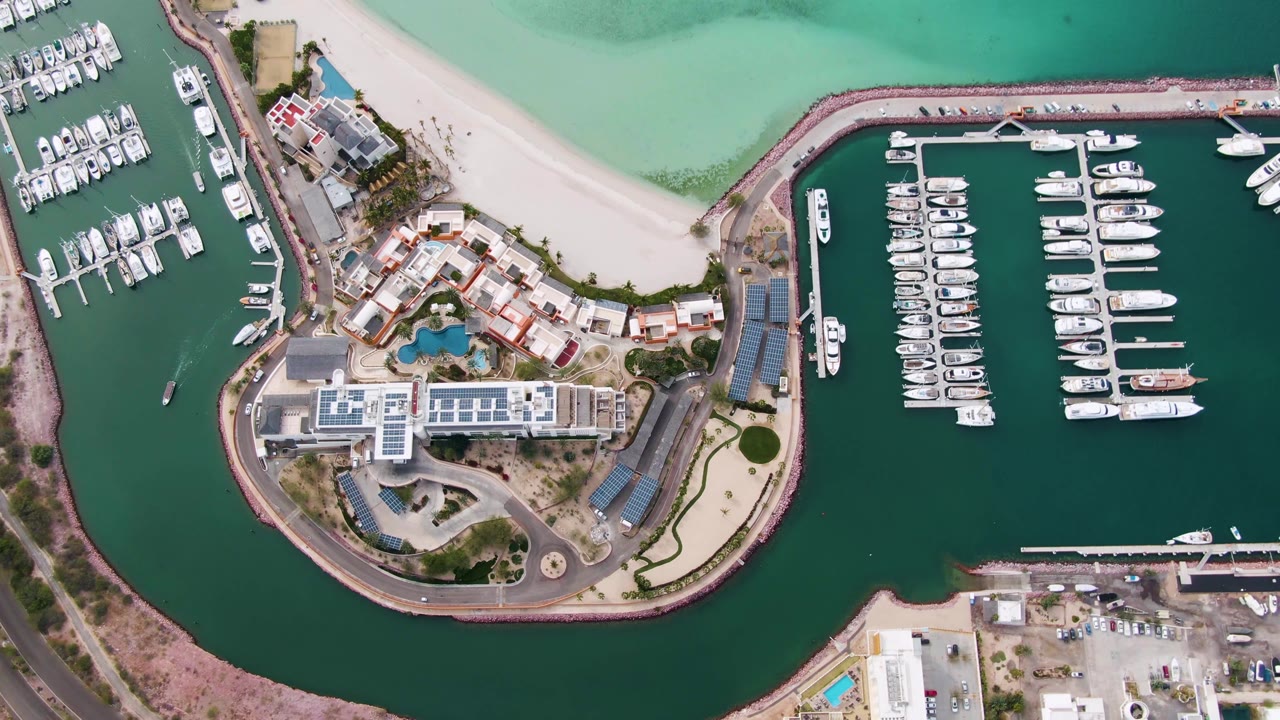 Static overhead marina view with docked yachts and sandy beach.