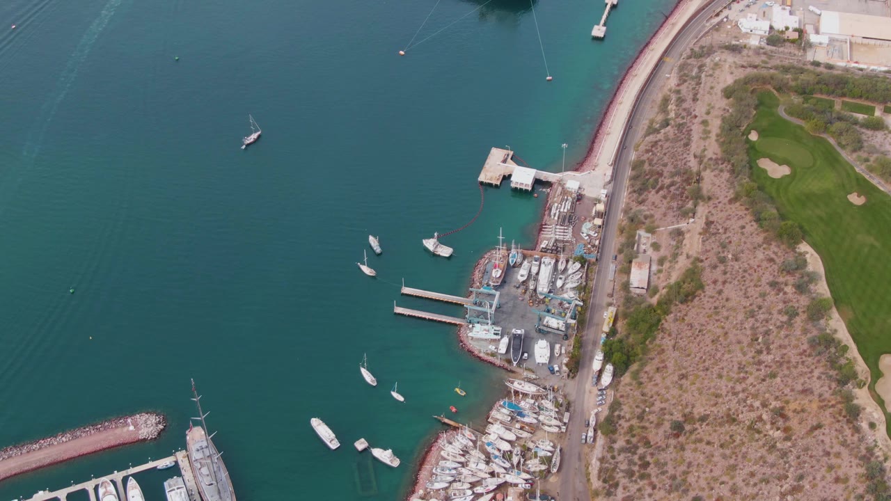 Aerial view of harbor water, docked boats, shoreline road, and green grass