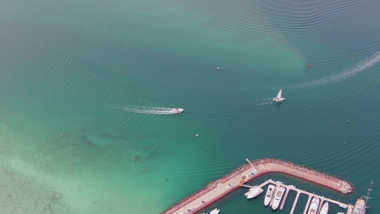 Aerial frame from La Paz, Baja California Sur, Mexico with the motorboat slightly farther across the water, the sailboat to the right, faint ripples, buoys, and no visible people.