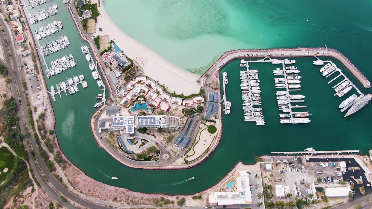 Overhead marina and beach with road and docked boats along green water.