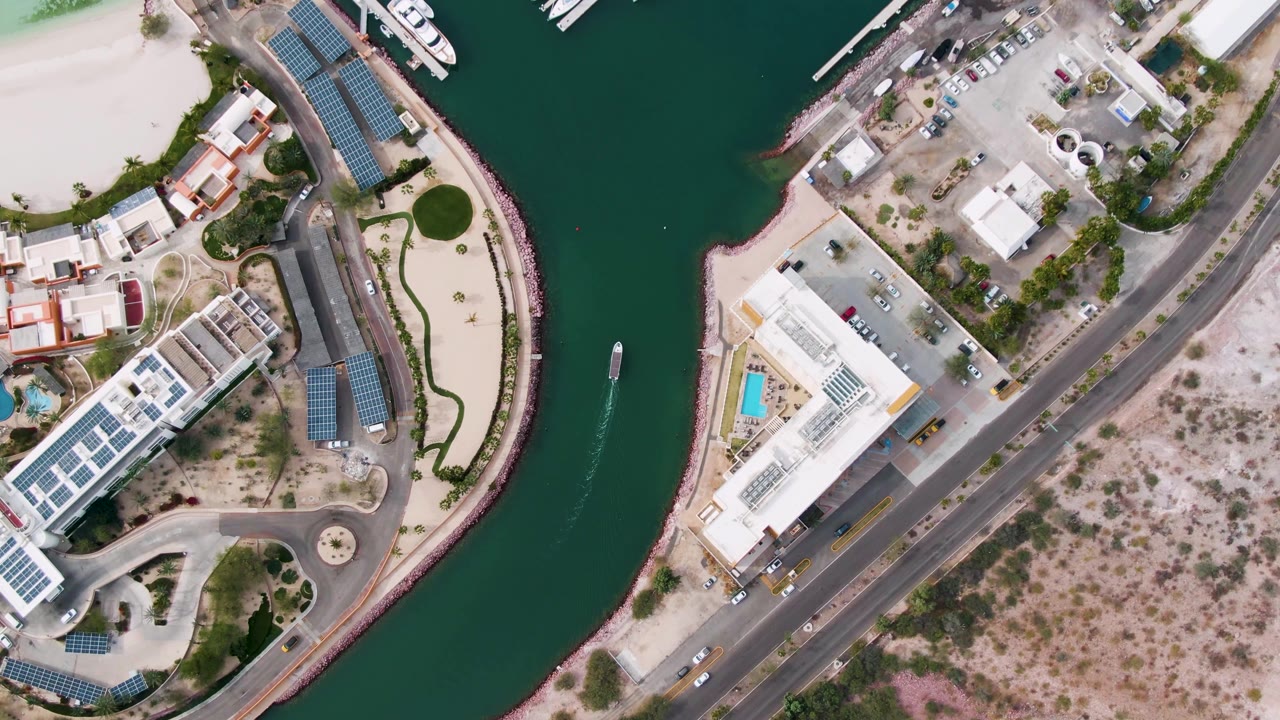Overhead canal curve with boat, docks, white buildings, road, cars, and sandy lots.