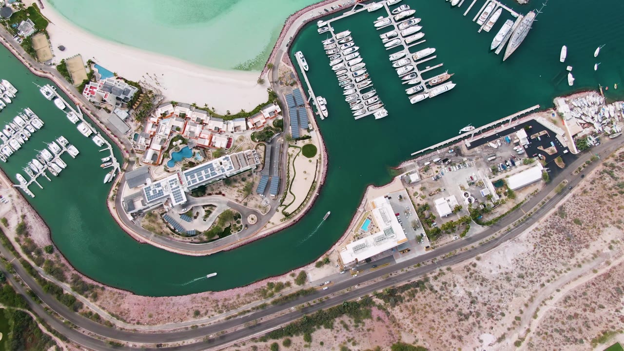 Aerial marina view with boat slips, beach, curved road, and shoreline buildings.
