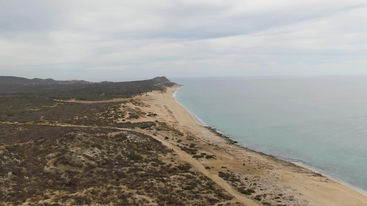 Aerial view of Punta Gorda Beach in Baja California Sur with sandy shoreline curving beside pale blue water, scrubby inland hills, and no visible people.