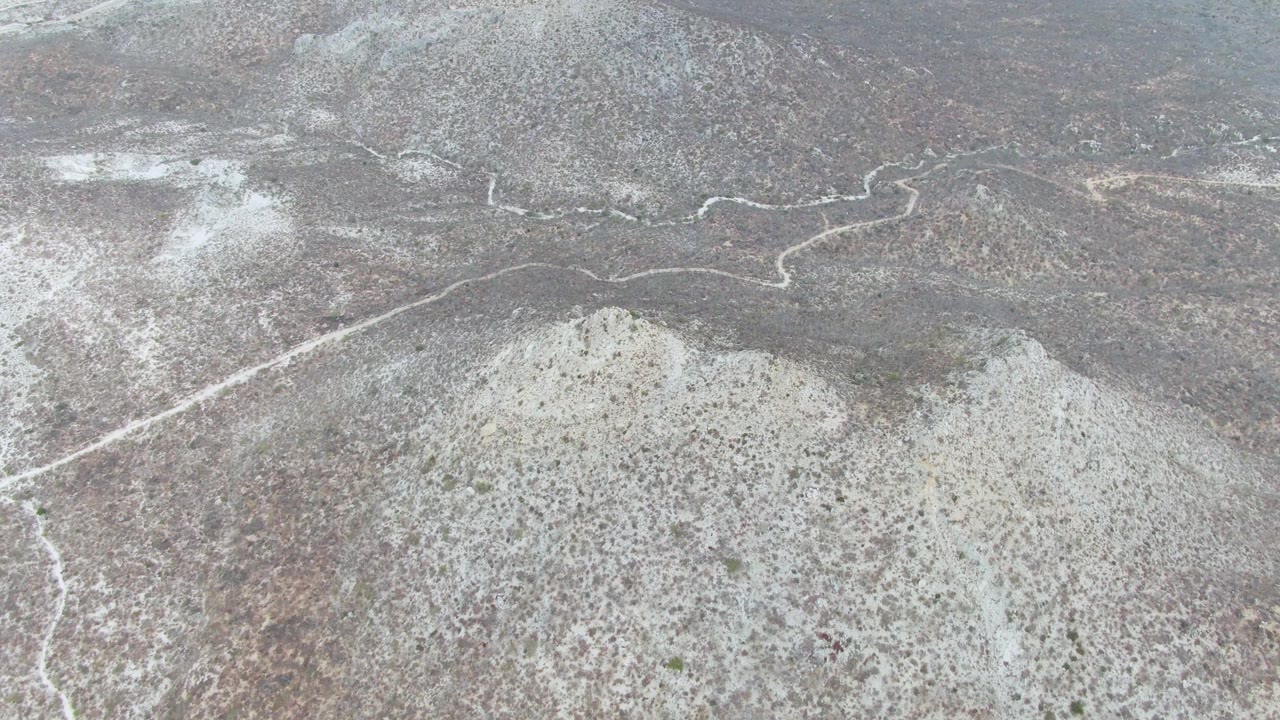 At 0:00, an elevated view over Punta Gorda Beach, Baja California Sur shows a pale winding riverbed feature cutting through gray-brown scrubland with no visible people.