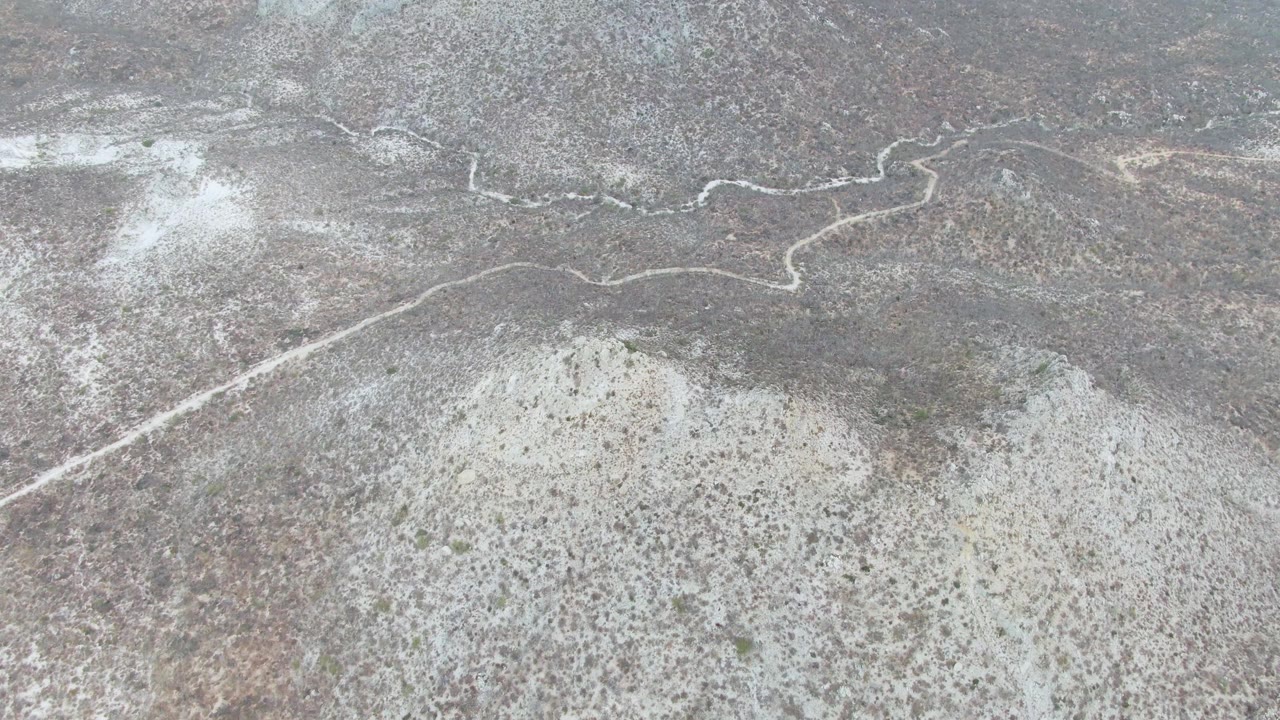 Aerial view over Punta Gorda Beach, Baja California Sur terrain, with a pale dirt road curving through gray-brown desert scrub and no visible people.