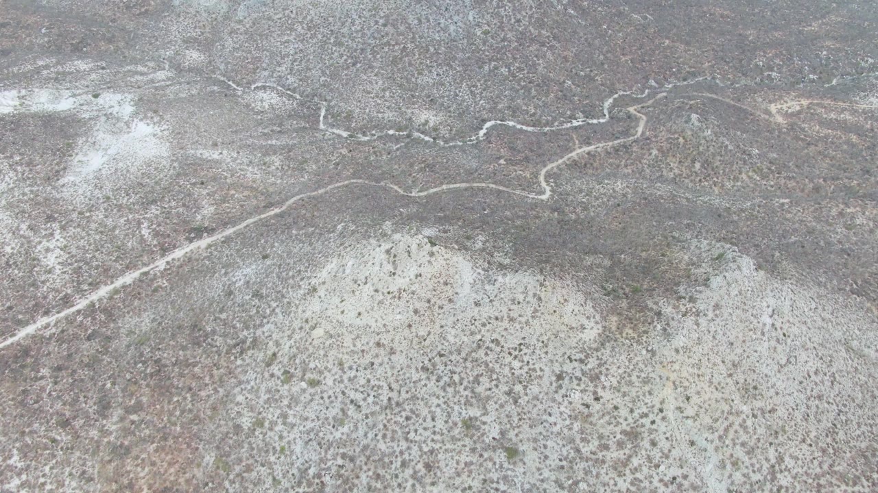 A slightly later aerial frame over Punta Gorda Beach, Baja California Sur, showing the dirt road bending across mottled dry ground with no visible people or vehicles.