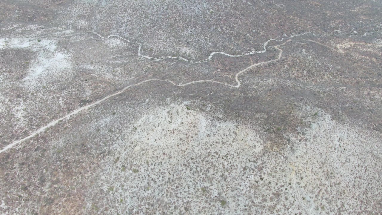 Aerial frame from Punta Gorda Beach, Baja California Sur, with a pale road line snaking across rocky scrubland and no visible people in the open terrain.