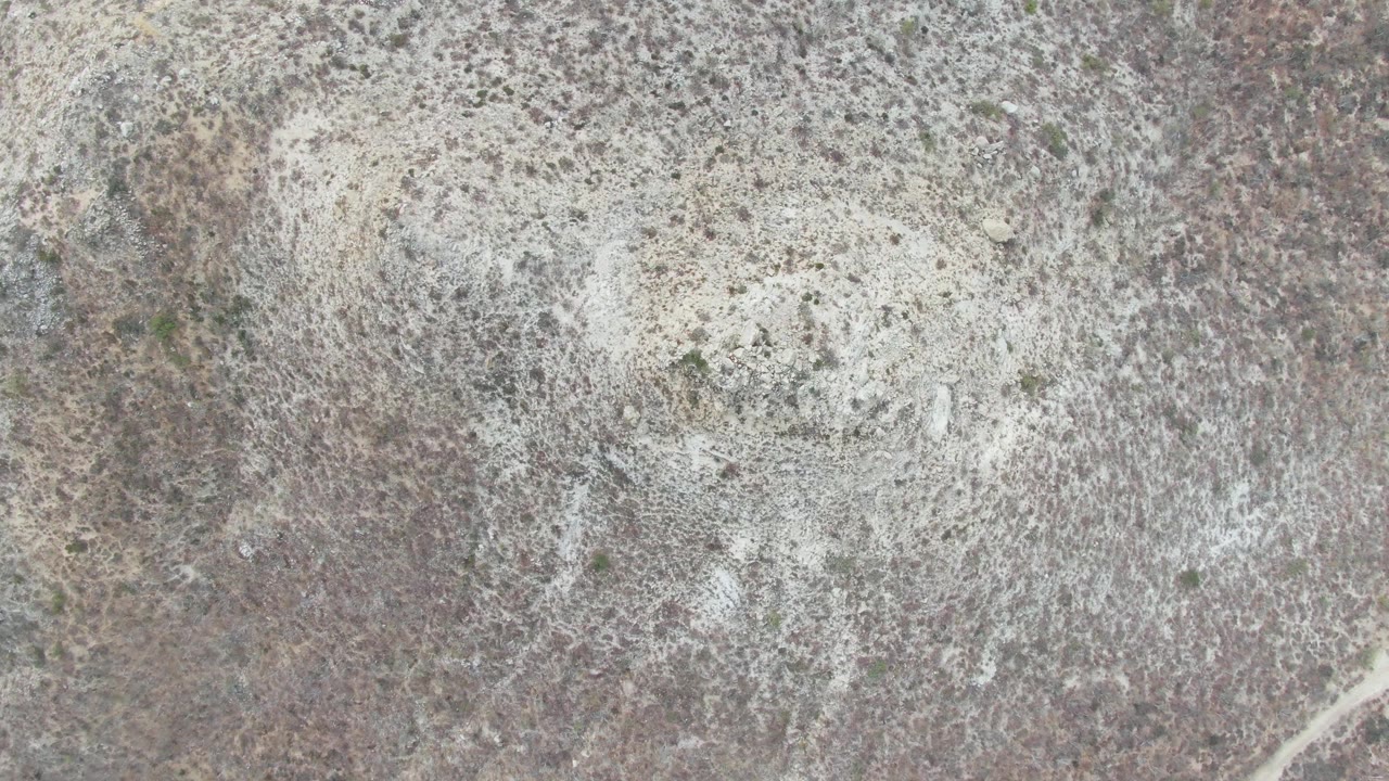 Third overhead frame at Punta Gorda Beach, Baja California Sur, showing a broad pale mineral area on textured rocky soil with scattered vegetation and no visible people.
