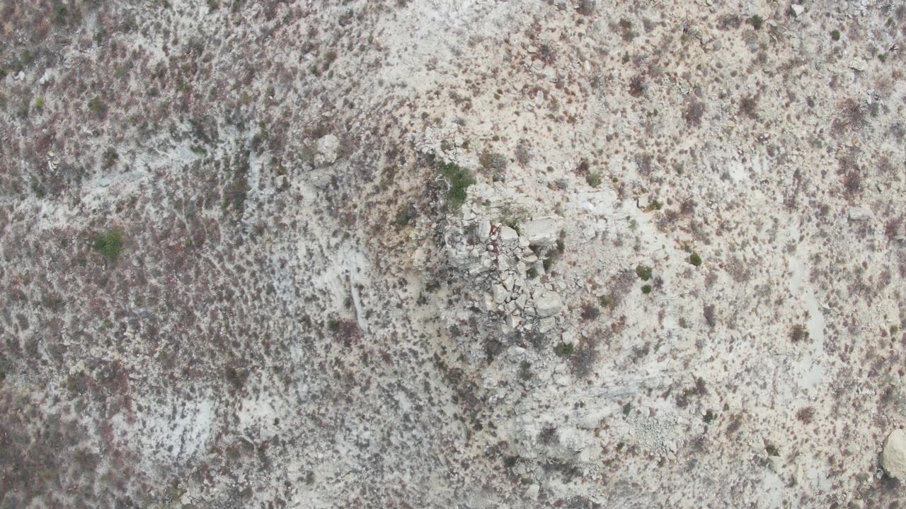 A direct overhead frame from Punta Gorda Beach, Baja California Sur, showing dry scrub, light stone clusters, pale soil, and no visible people as the small object continues its slow movement.