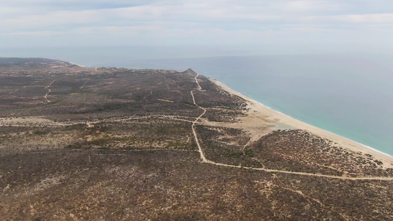 Aerial view over Punta Gorda Beach in Baja California Sur, with pale dirt roads crossing arid scrubland beside a sandy shoreline and blue-green water, no visible people.