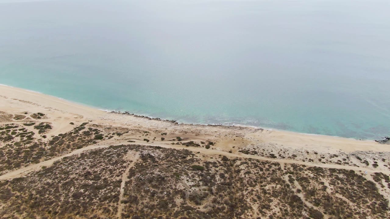 Aerial view of Punta Gorda Beach showing low scrub on the dunes, sandy tracks near the shore, a narrow line of waves, and no visible people.