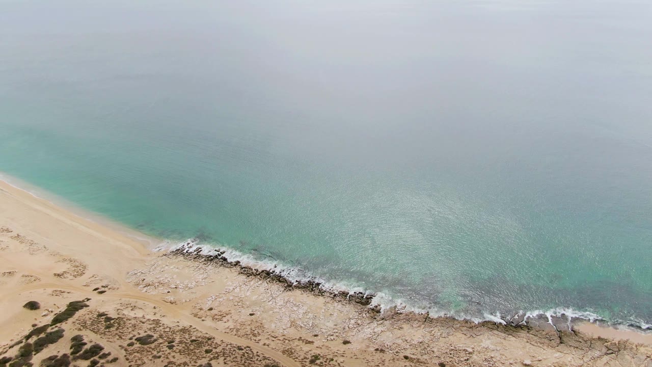 Aerial view of turquoise surf meeting sandy and rocky shoreline