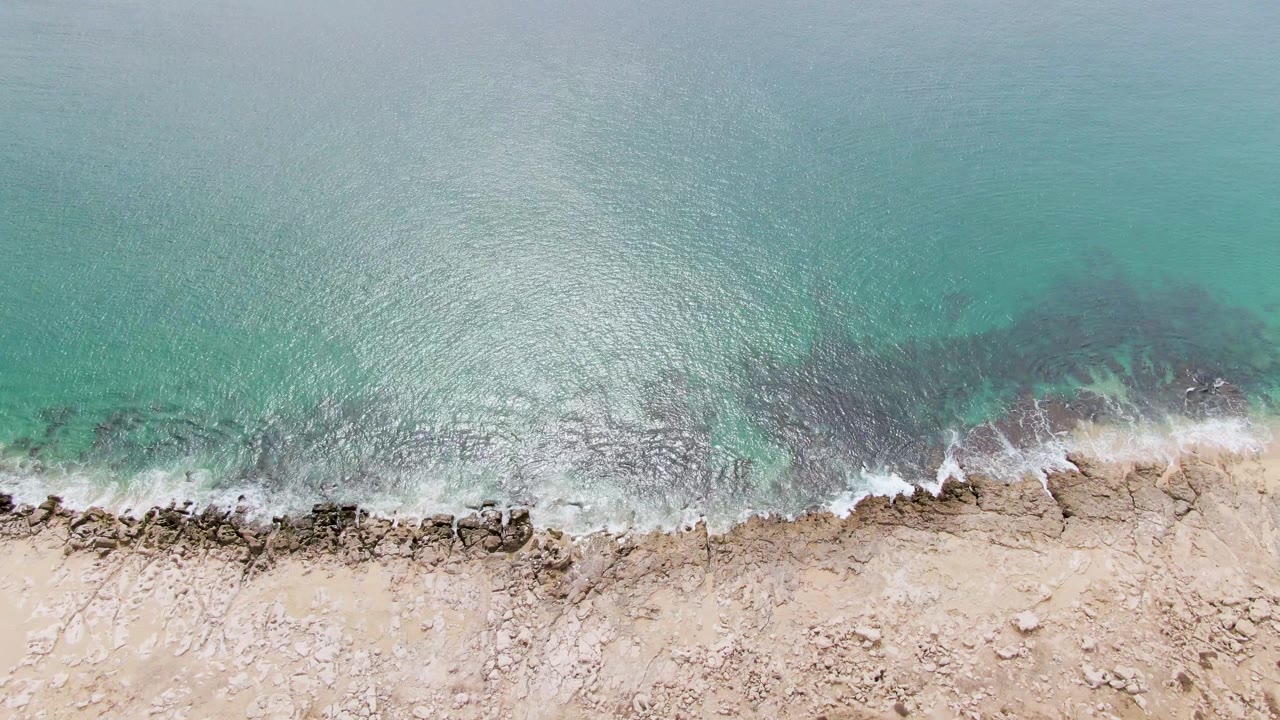 Top-down view at Punta Gorda Beach where white foam gathers along a rough rocky section below turquoise water, with no visible people.