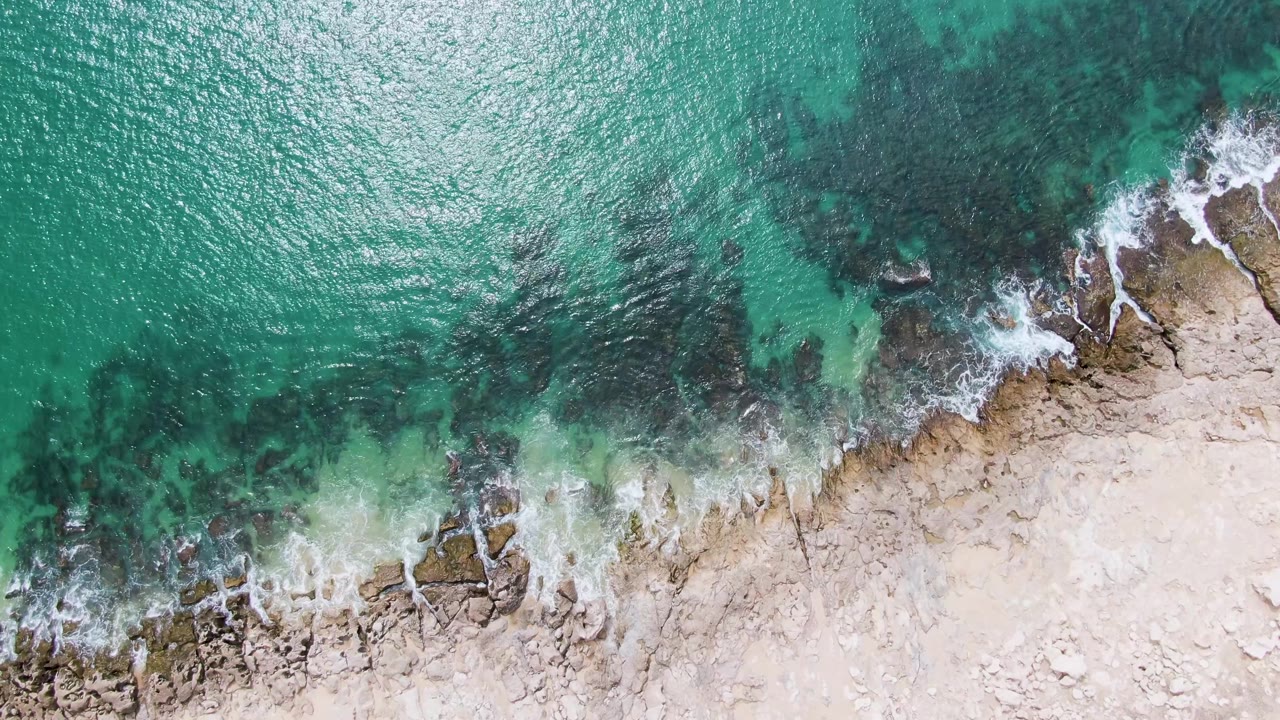 Overhead ocean and rocky shore with foam near the waterline.