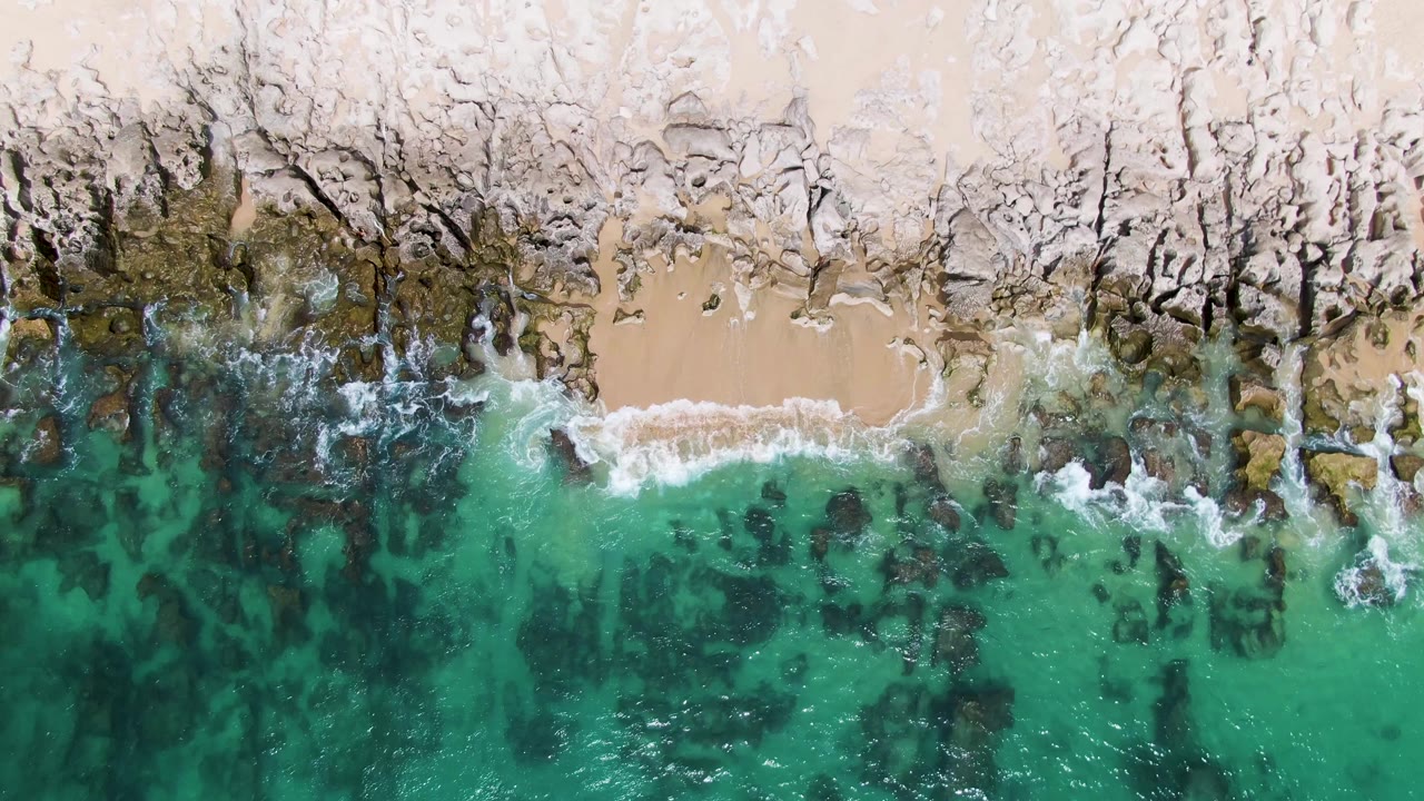 Overhead view of turquoise water meeting a rocky sandy shore.