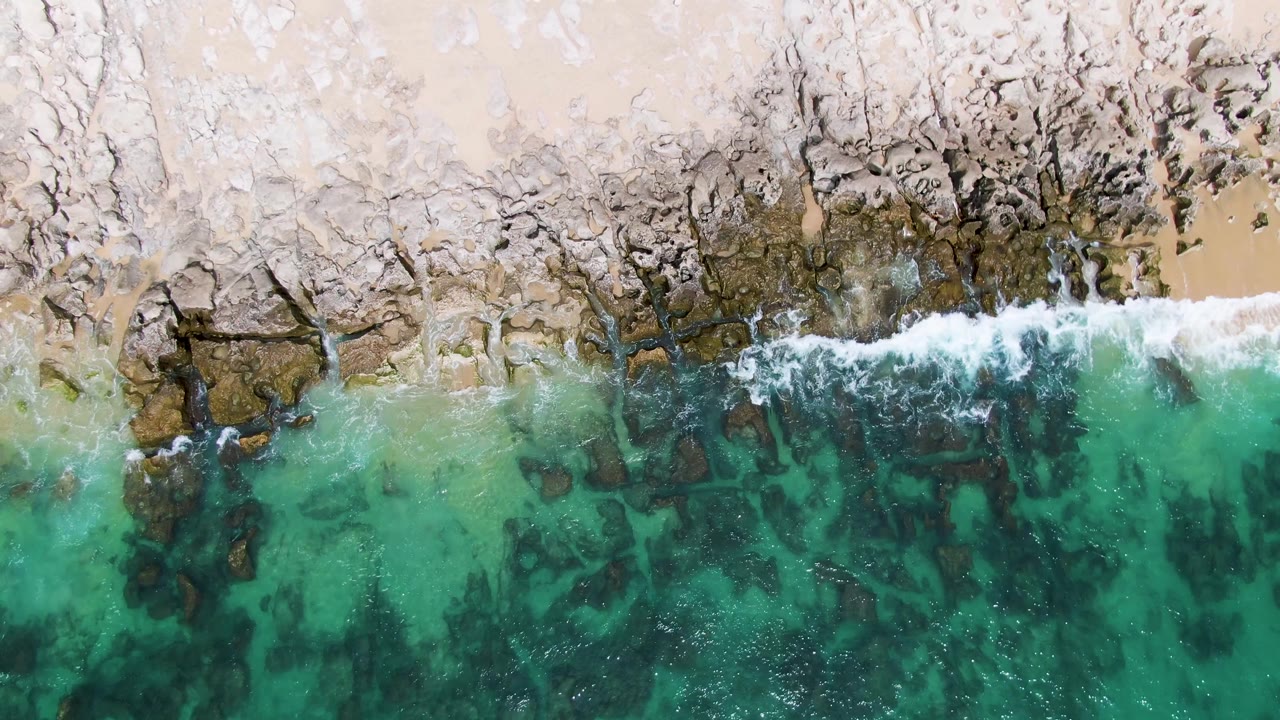 Overhead turquoise water meeting a rocky sandy shoreline