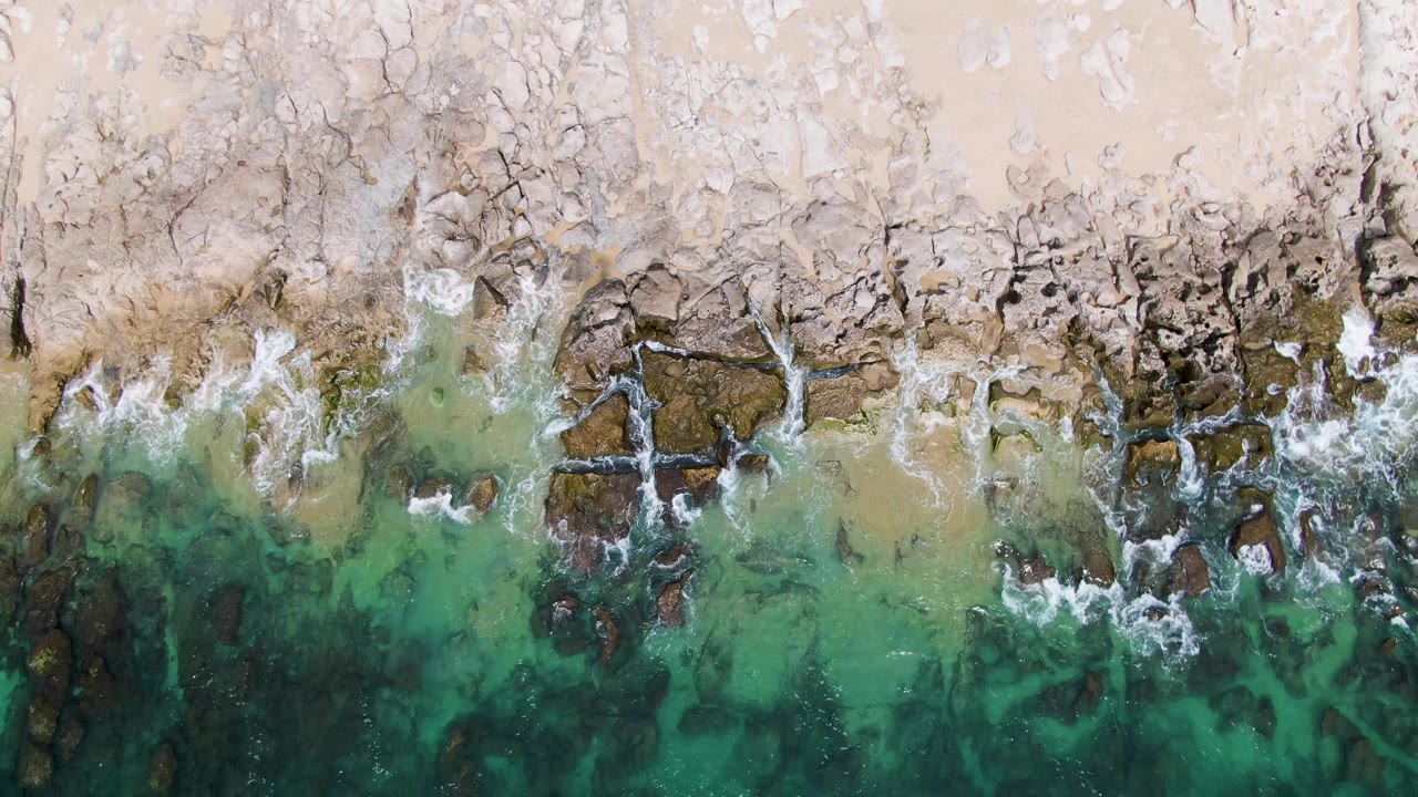 At 0:01, Punta Gorda Beach is seen from above as white surf spreads over darker rock patches beneath green-turquoise water, with no visible people.