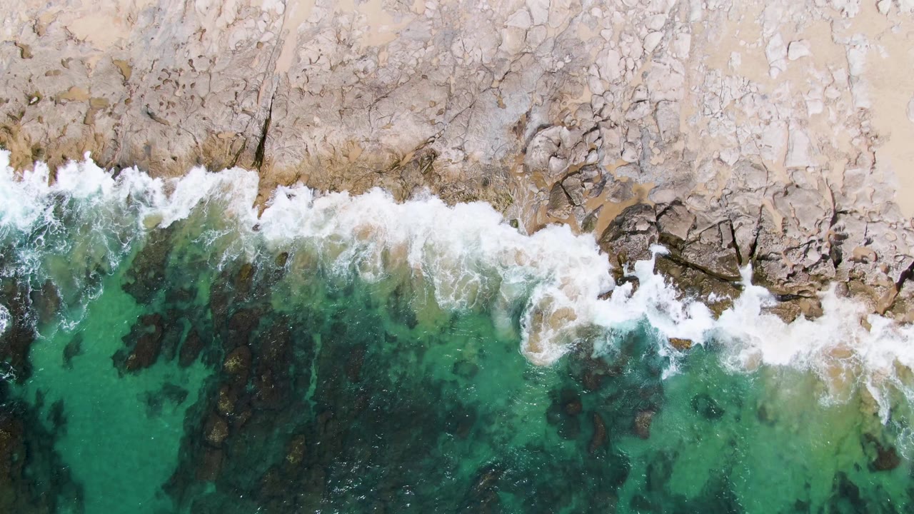 White surf curling across rocks beside turquoise water