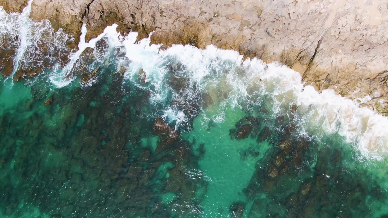 Overhead turquoise water and white surf breaking on tan rocks