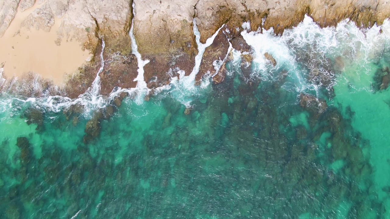 White surf spreading over rocks beside clear green-blue water.