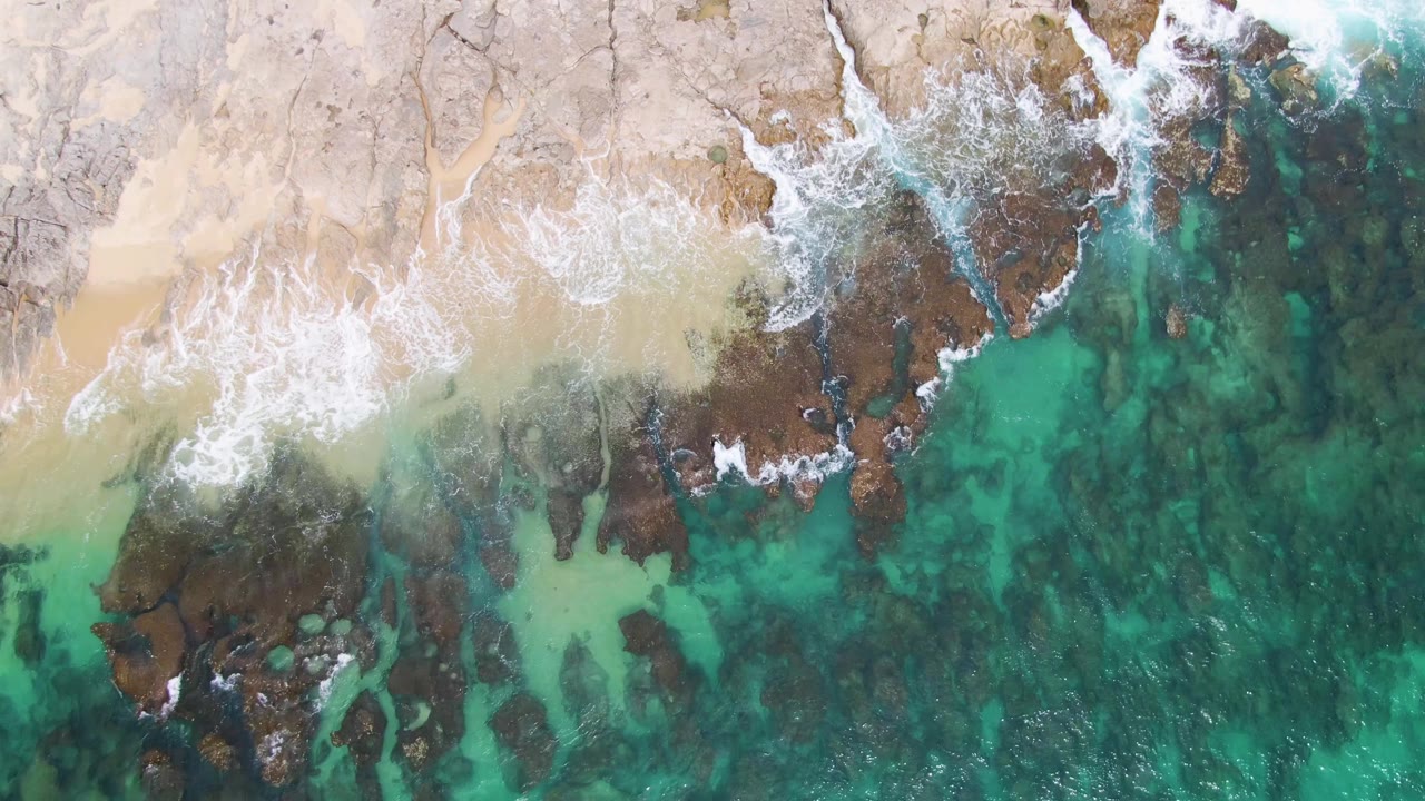 Wave wash crossing sand and dark rocks in turquoise water